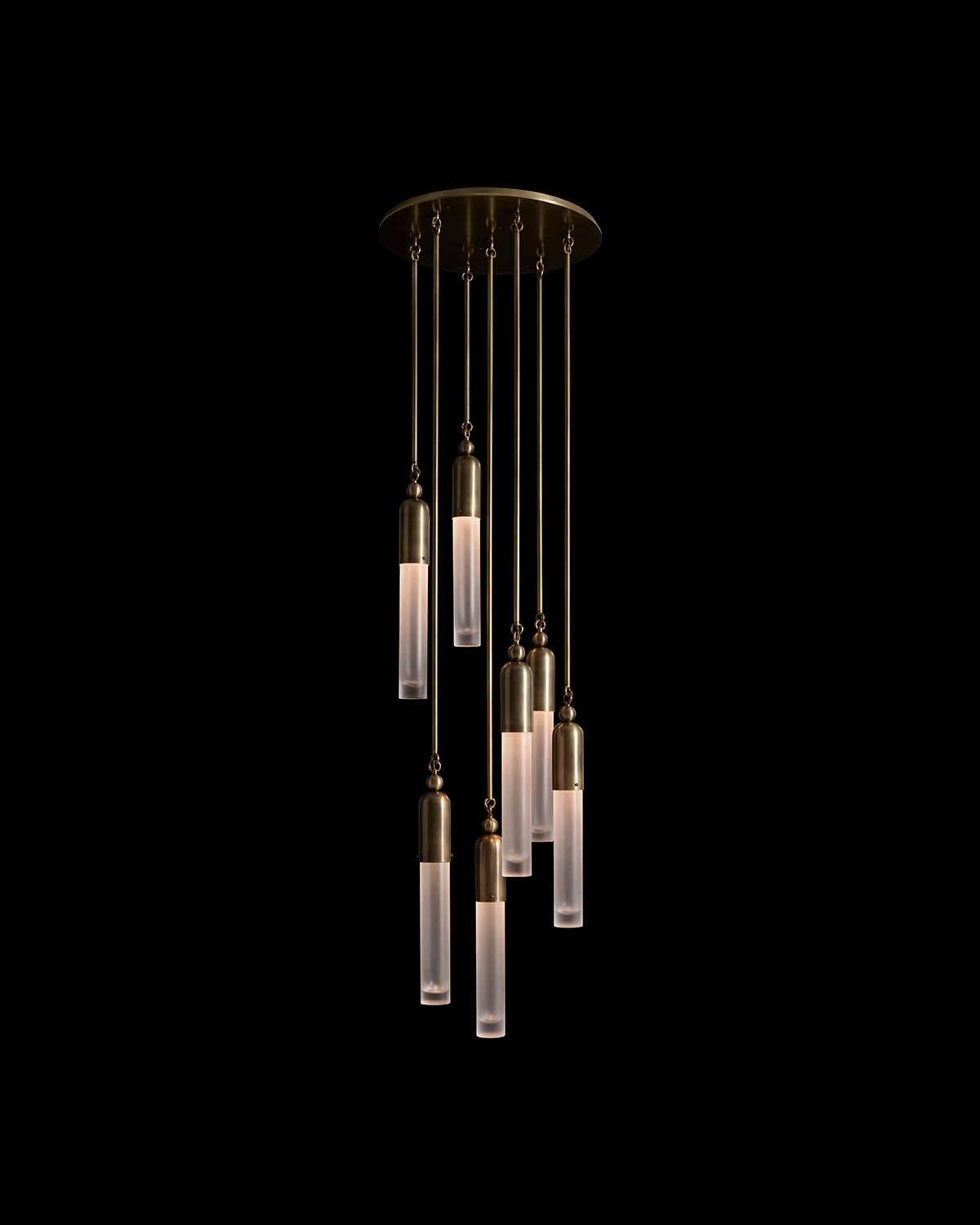Six slender pendant lights with frosted glass tubes and brass accents hanging from a circular ceiling mount on black background