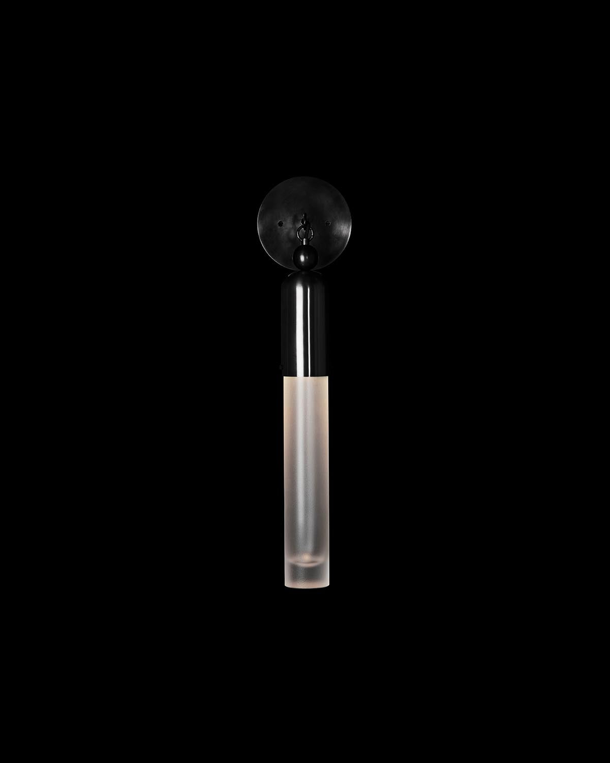 Minimalist vertical wall sconce with matte black circular base and frosted elongated glass shade on black background