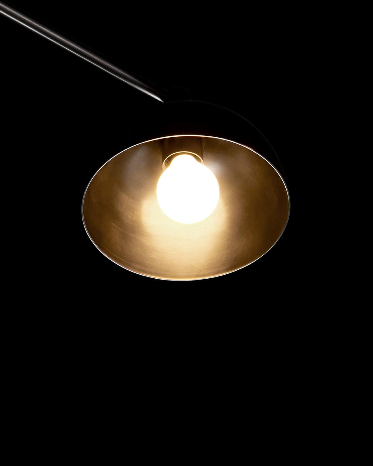 Close-up of a single illuminated bulb inside a black dome-shaped lamp shade against a dark background