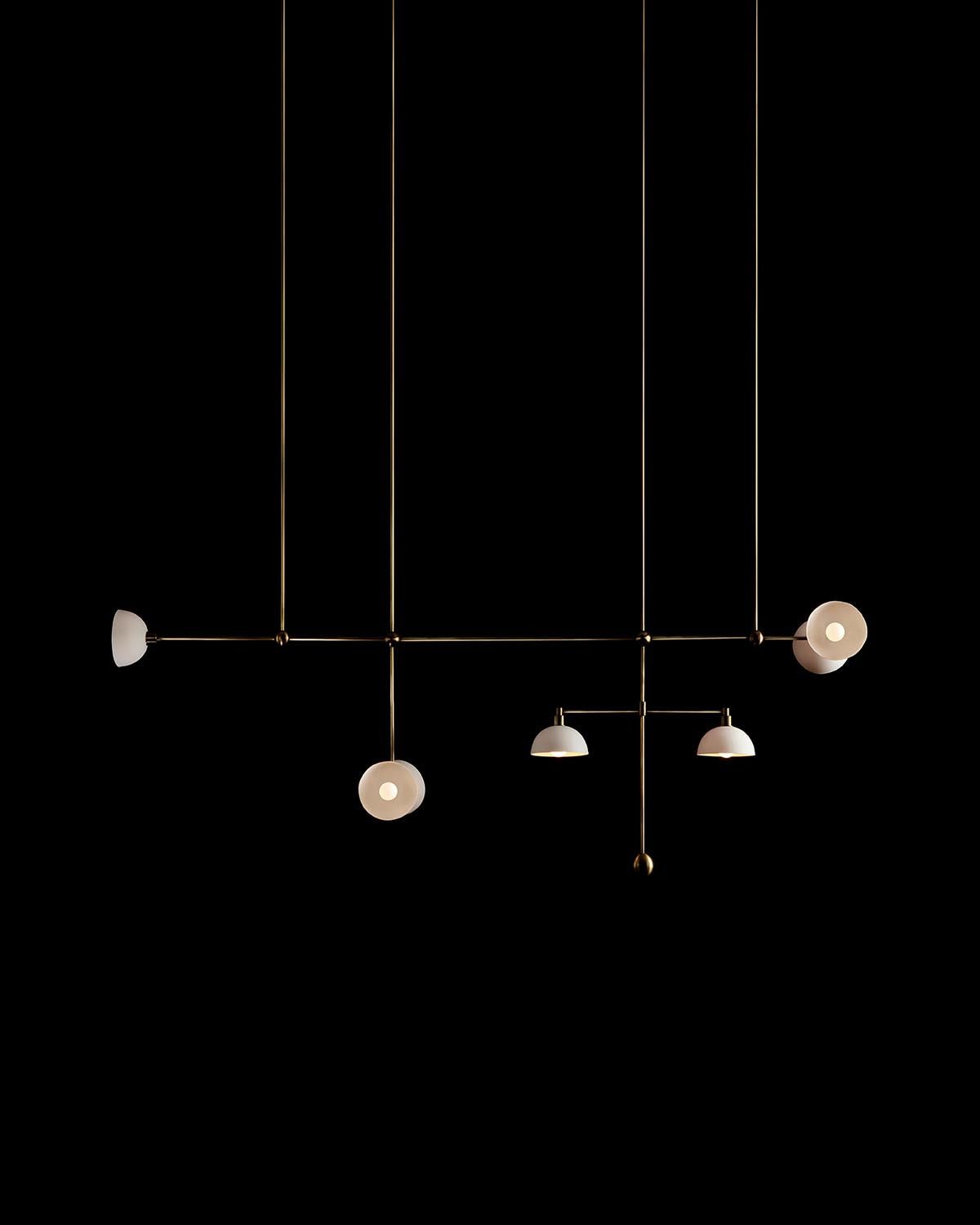Minimalist metal pendant light fixture with five asymmetrical white shades suspended against a black background