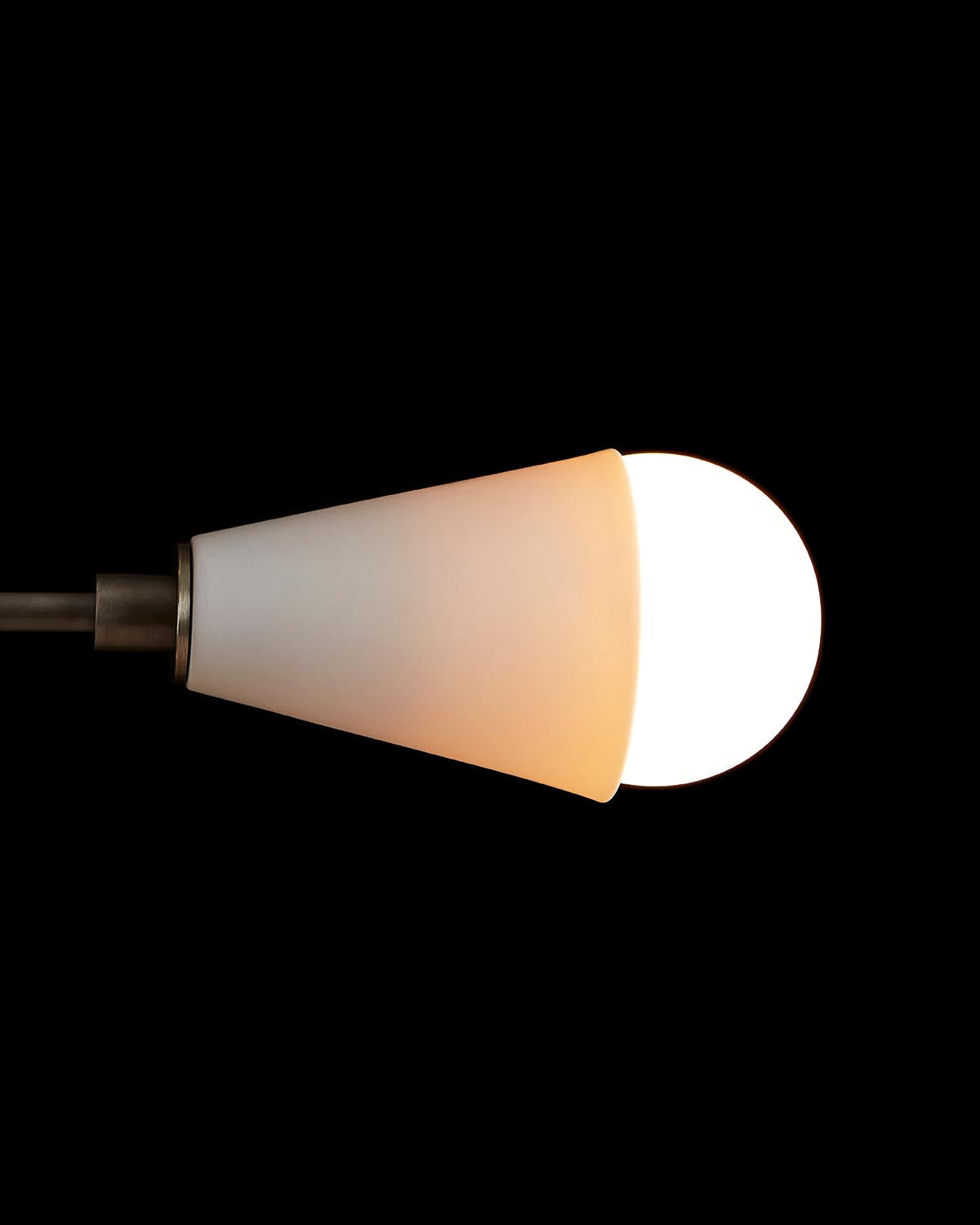 Close-up of a modern pendant light with a frosted cone-shaped shade and glowing round bulb on a black background