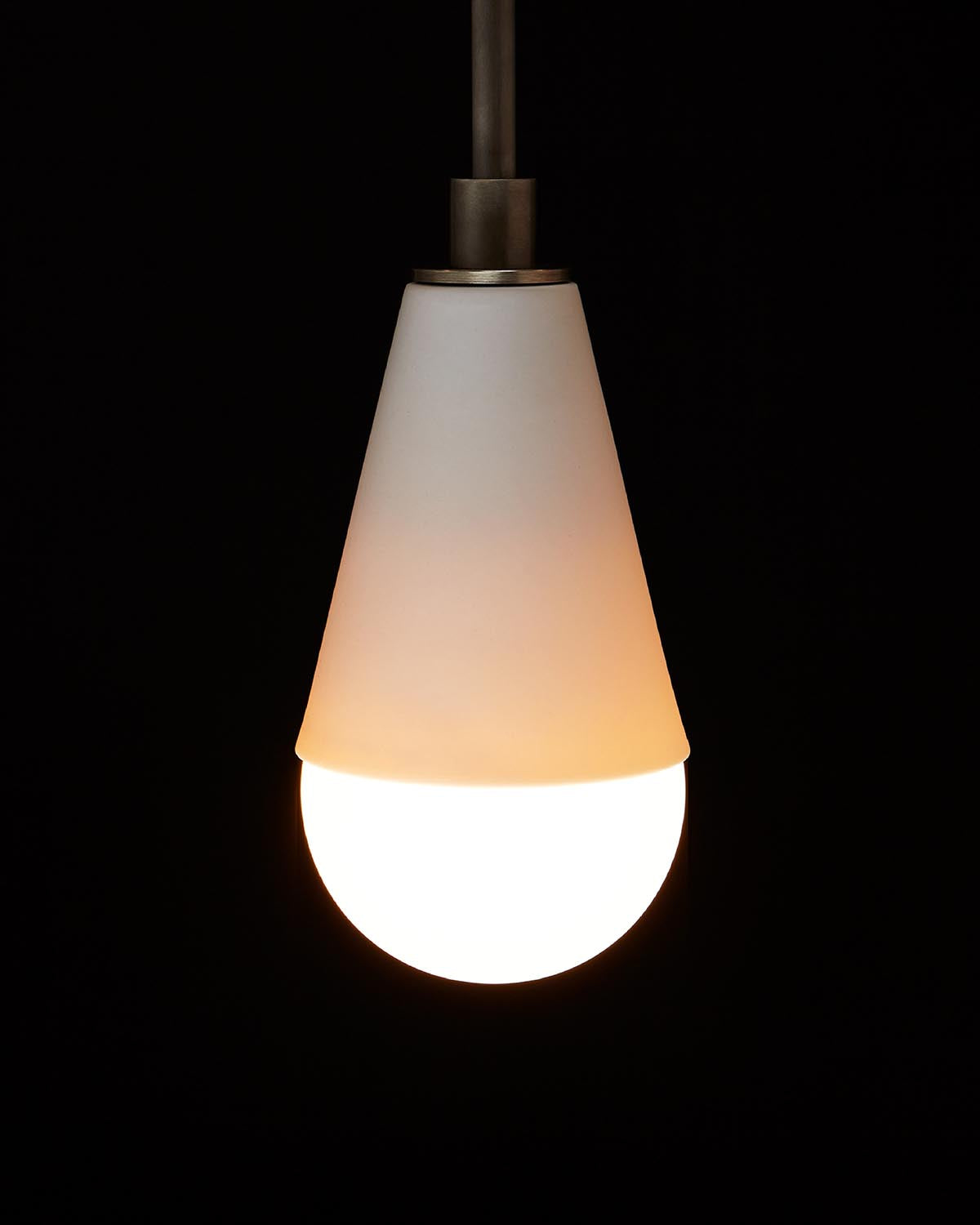 Minimalist pendant light with white conical shade and illuminated round bulb against a black background
