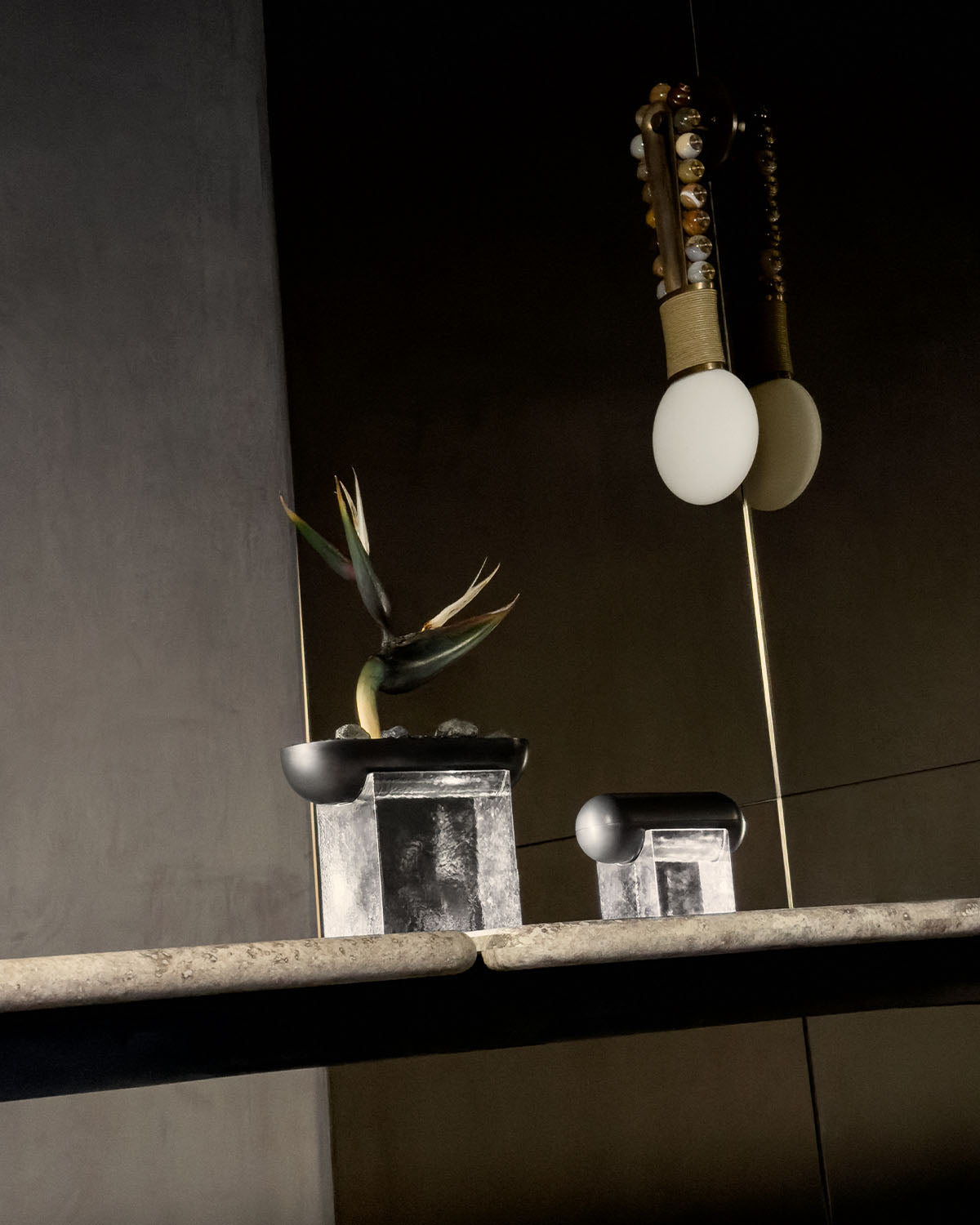 Minimalist stone and metal vessel with dark rounded tops displayed on a textured stone surface against a muted backdrop